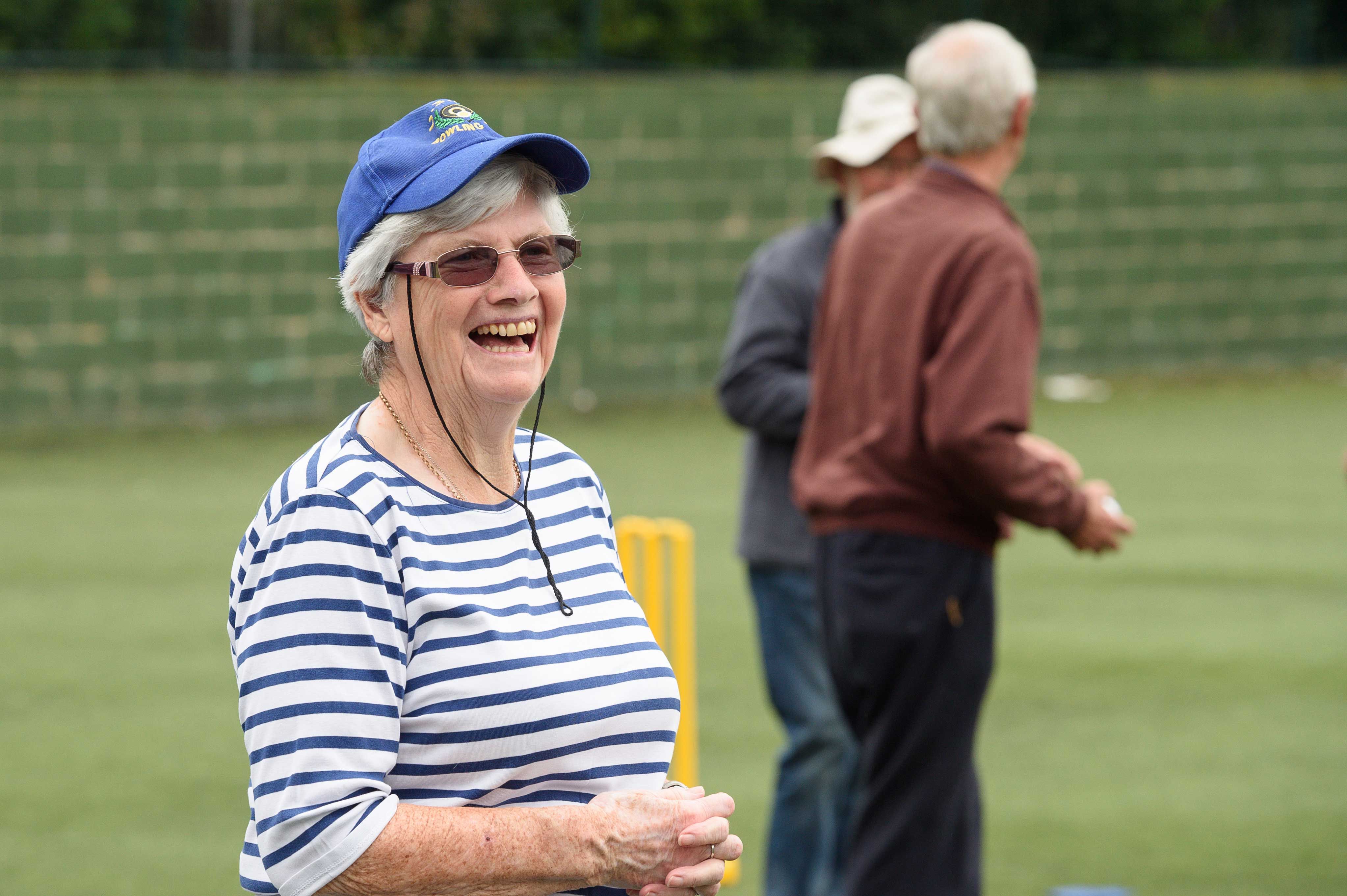woman smiling to right of camera in front of two adults and a set of cricket stumps