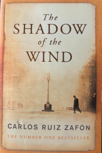 The book cover of The Shadow of the Wind. The book is a faded brown colour and shows the silhouette of a man walking in a city at night.