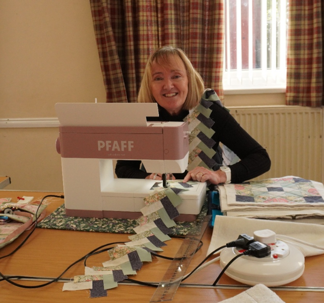 A woman sat at a table in front of a sewing machine, making patchwork