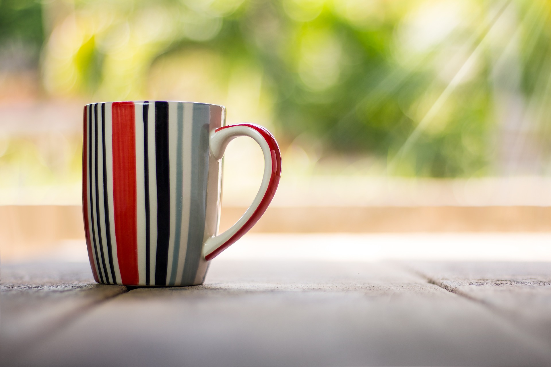 A colourful stripy mug outside with sunshine rays coming down on it 
