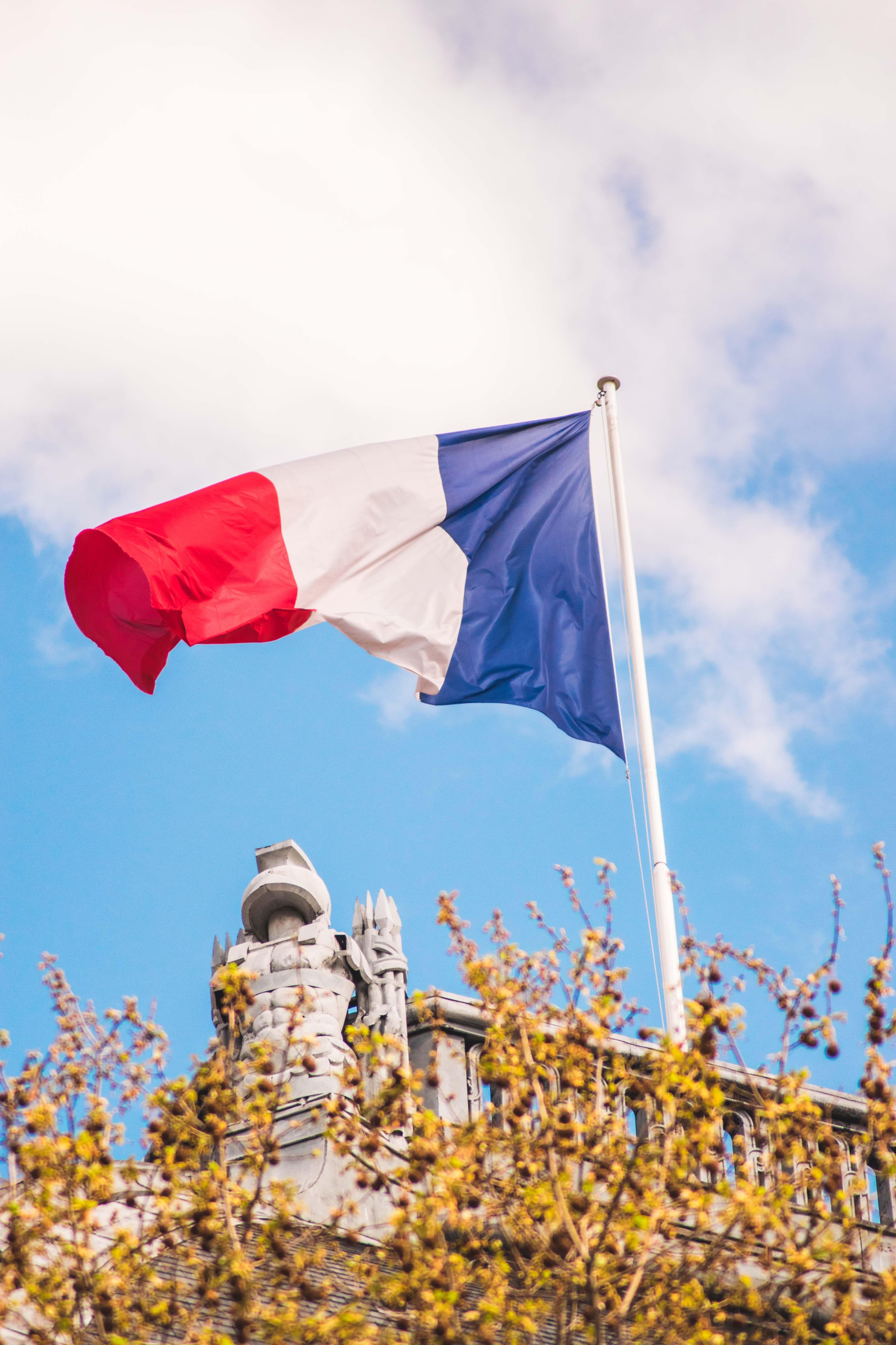 french flag flying on a pole against bright blue sky with cloud