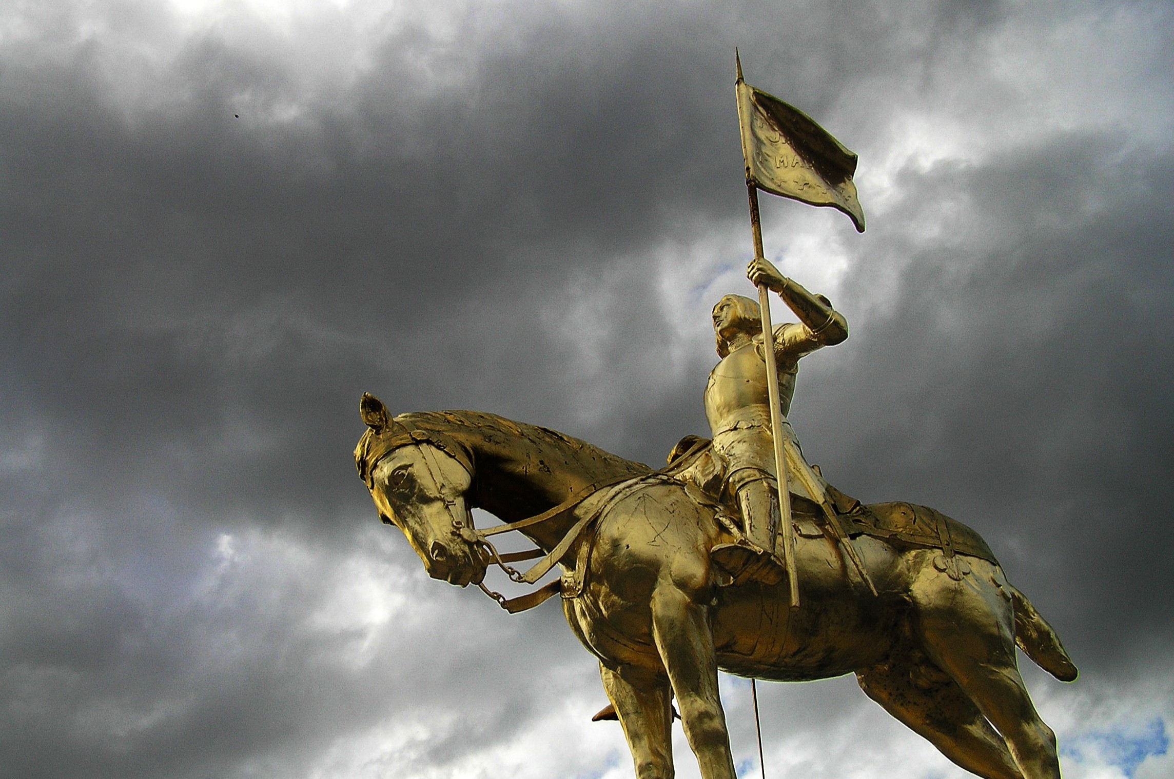 gold statue of joan of arc against grey cloudy sky