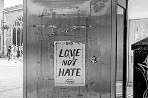 black and white photo of a phone box with a 'love not hate' poster on