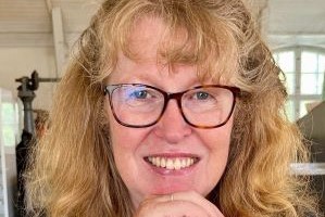 a woman with dark blonde curly hair and glasses smiling