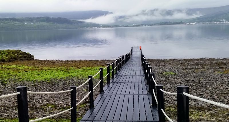 A lake with misty clouds on the horizon, with a jetty leading into the lake. The scene is calm