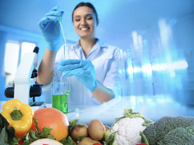 scientist holding test tube and pipette with vegetables in the foreground
