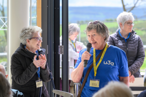 A volunteer speaking at an event with another member clapping