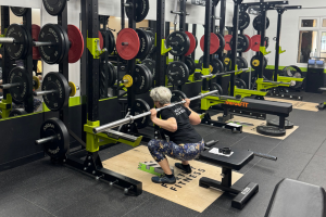 A woman with short grey hair is squatting whilst holding a barbell
