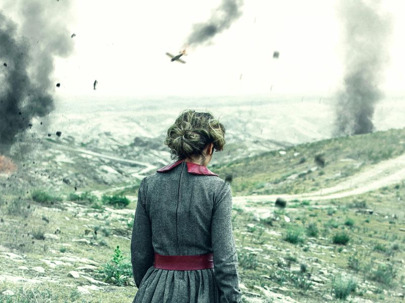 Photo of a woman walking through a landscape with a plane and smoke