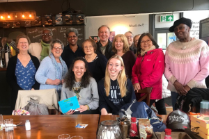 Two young women sit in front of a group of u3a members - everyone is looking at the camera and smiling