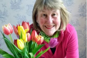 Woman standing in front of a vase of flowers and several books saying Nellie Bly